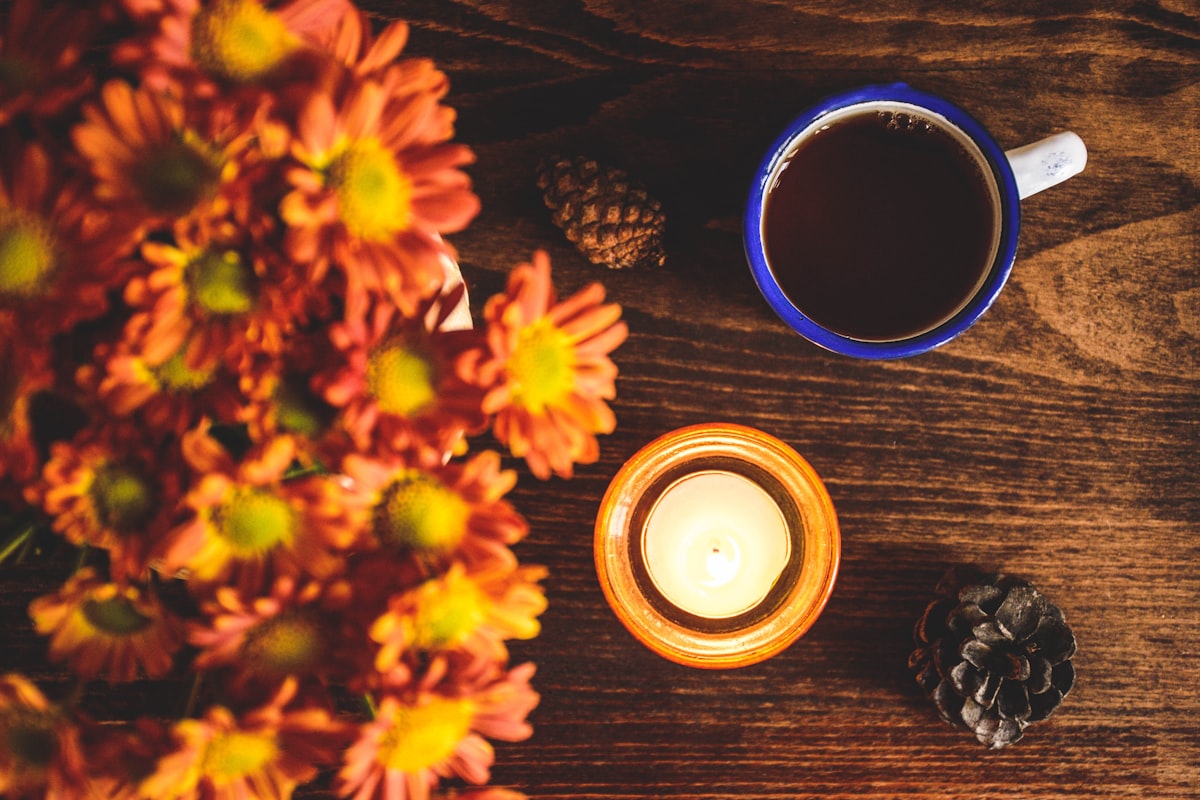 A warm mug beside yellow autumn flowers on a table, suggesting a quiet seasonal writing moment