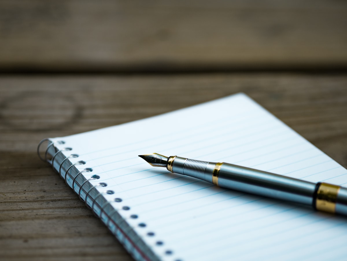 An open notebook beside a steaming cup of coffee, a pen waiting on a blank page for fiction to begin