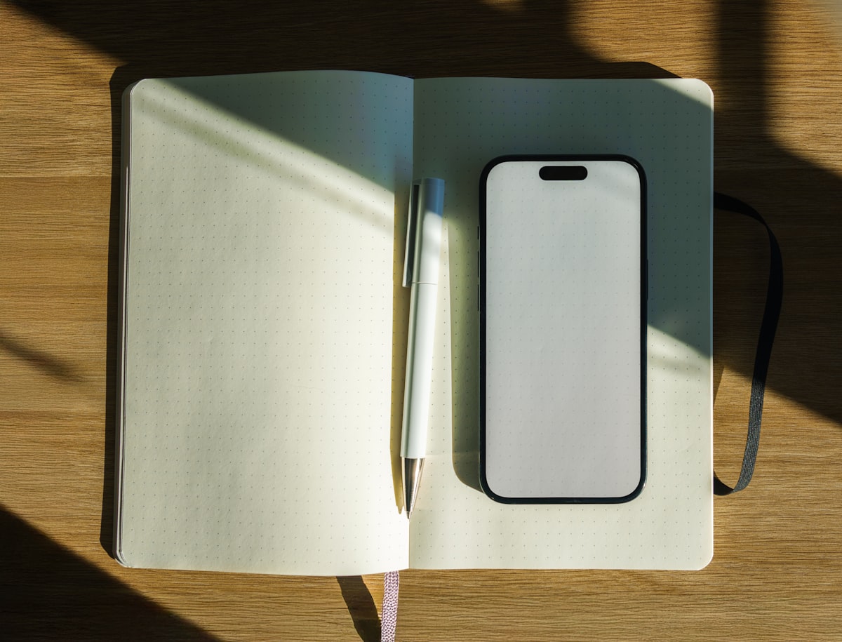 A paper notebook and a smartphone side by side on a clean desk, representing the choice between paper and digital diary writing