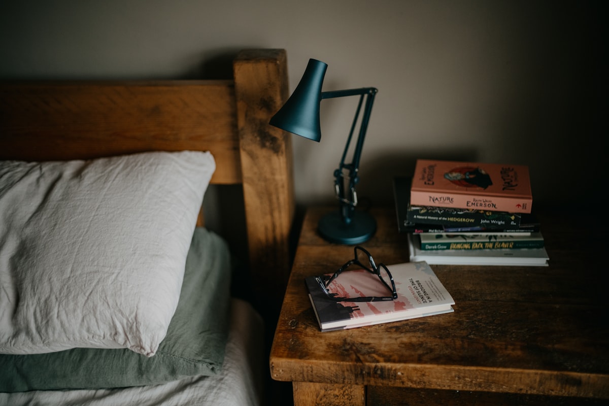 A stack of books on a bed next to a lamp, evoking bedside reading and writing