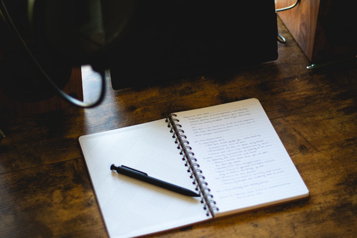 An open notebook with a pen lying across it on a wooden desk