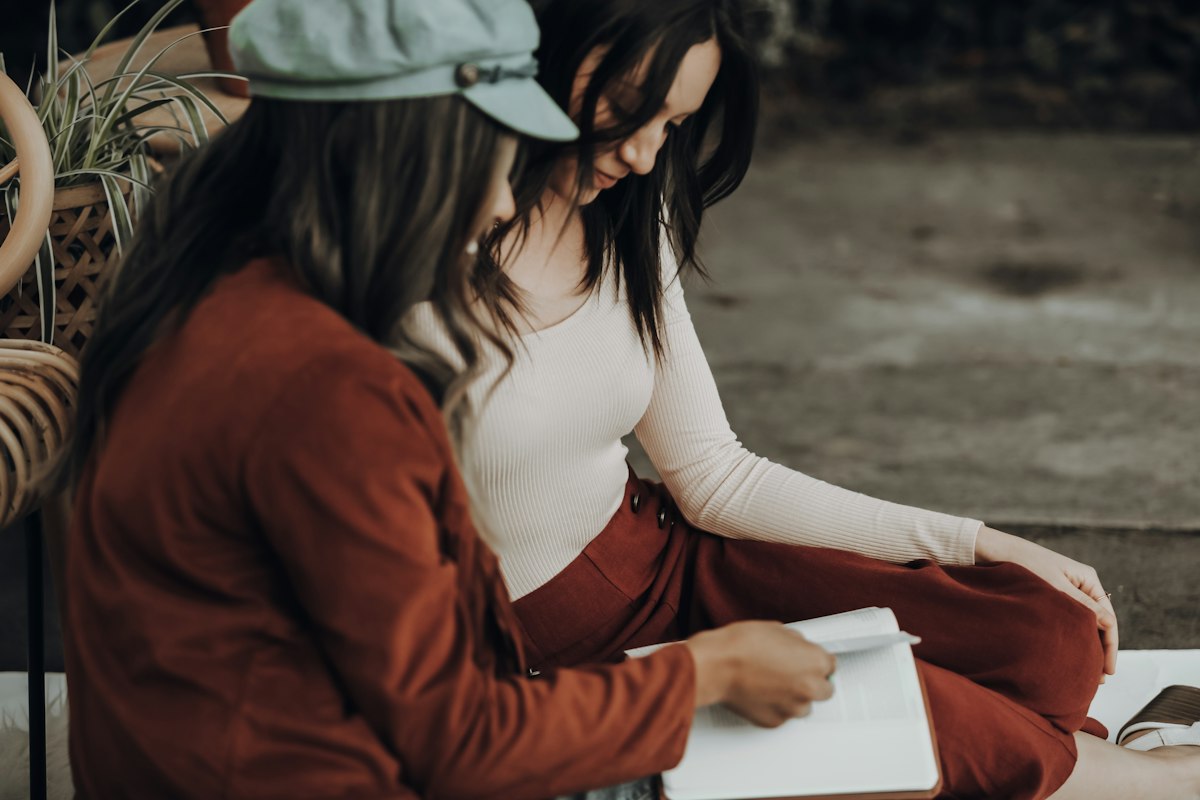 Two people sitting close together, one writing in an open notebook