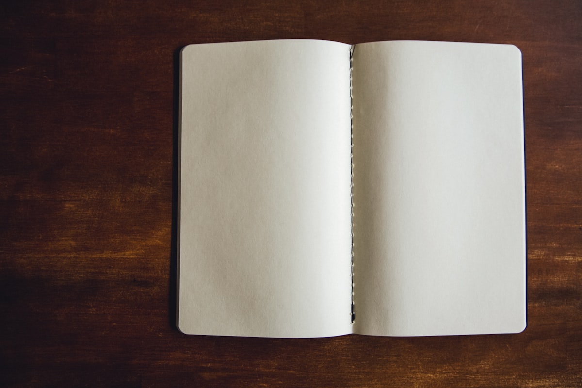 An open notebook and pen on a table beside a window, with steady daylight falling across the page