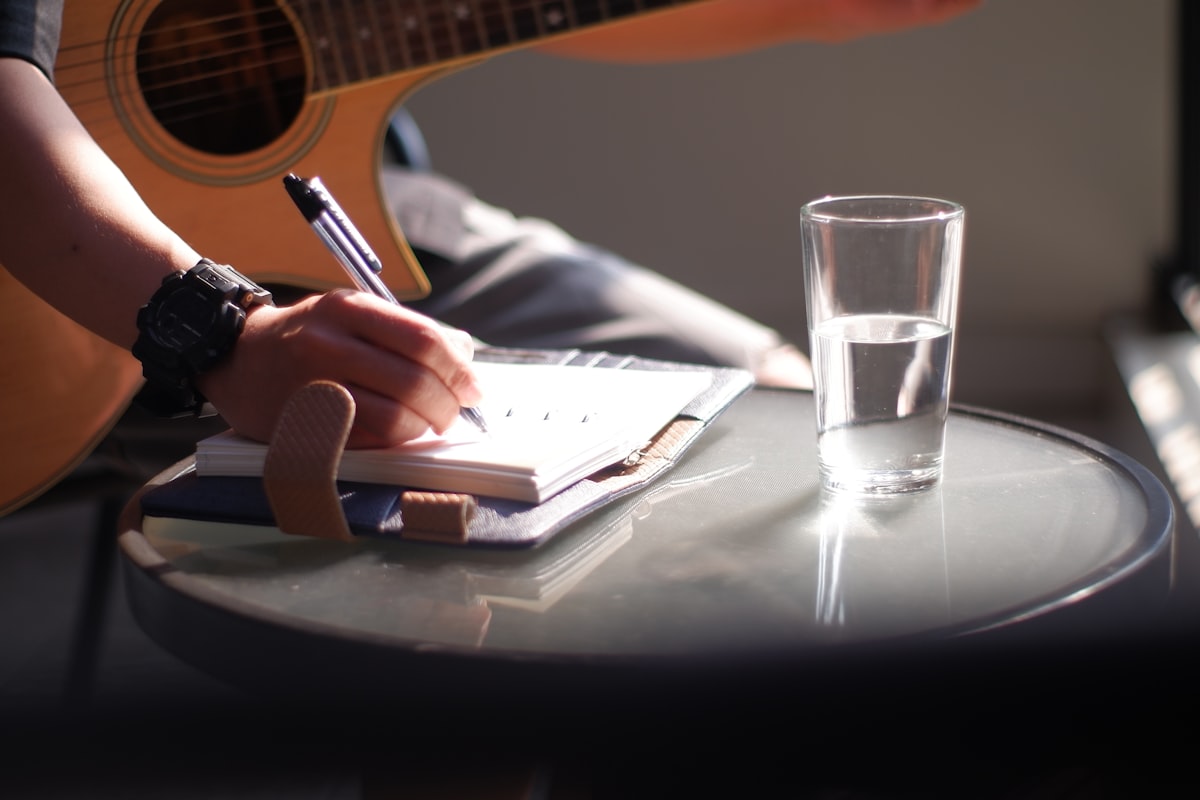 A person writing with a pen on white paper, suggesting a musician's working notebook