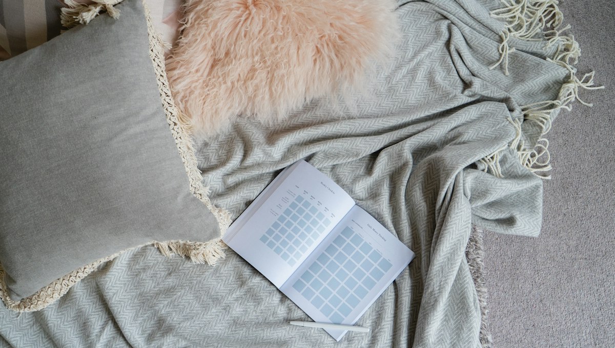 An open notebook resting on a soft knitted blanket beside a cushion