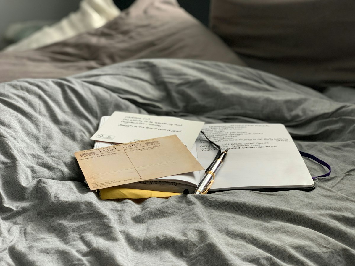 An open journal and pen resting on a bed with postcards tucked inside