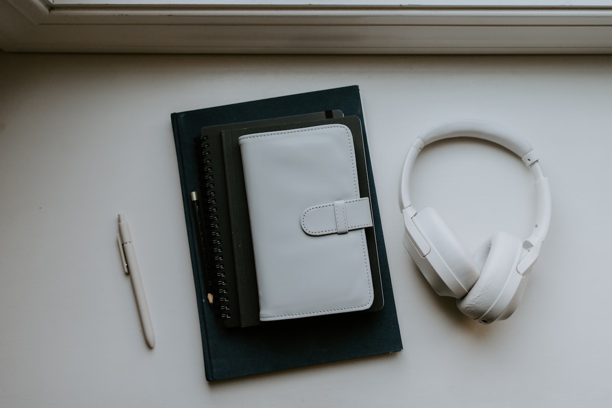 An open notebook on a desk beside headphones and a pen with warm lamplight falling across the page
