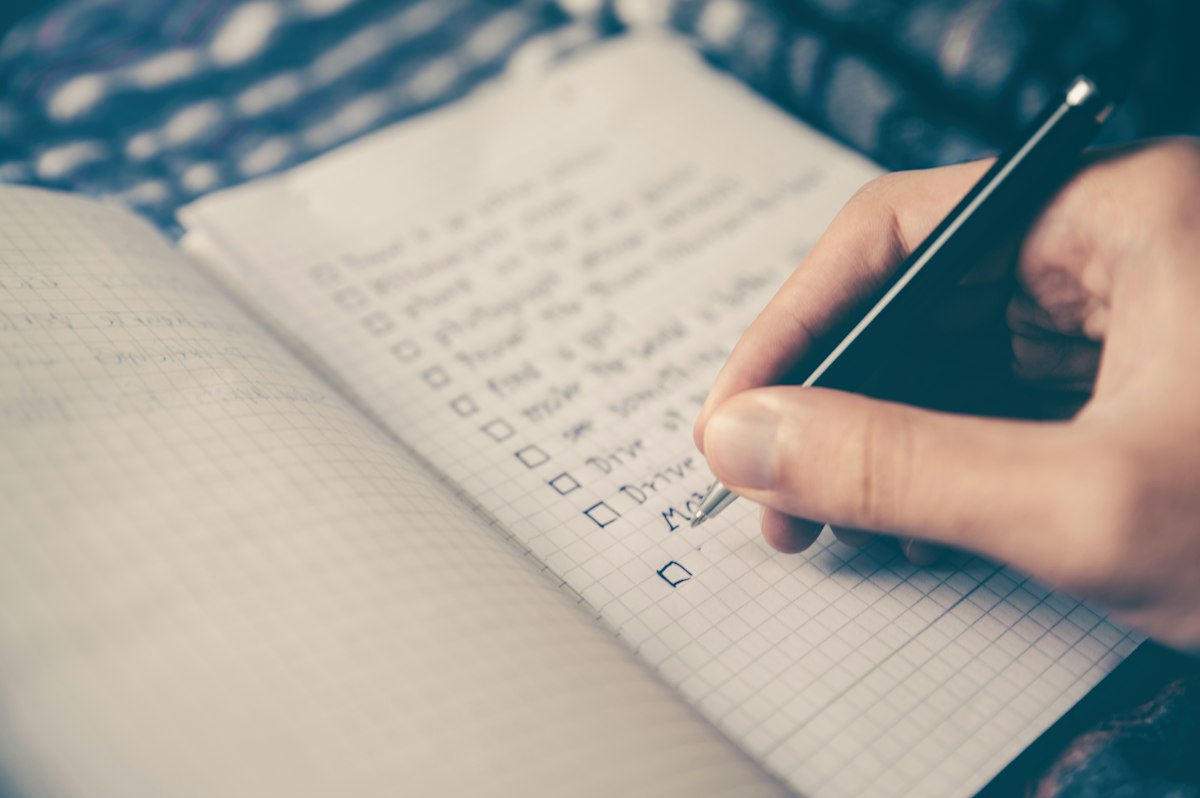 A person writing a handwritten list in an open notebook