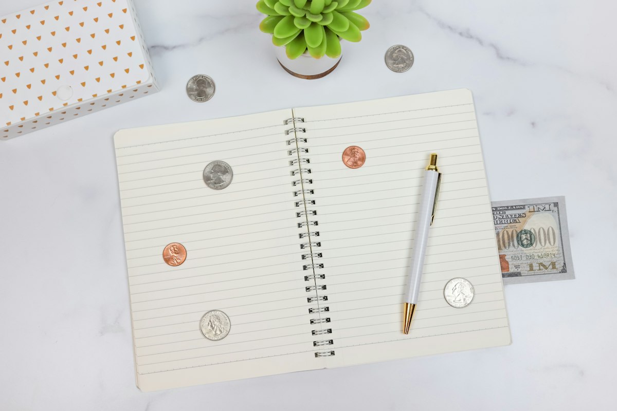 An open lined notebook with a pen and scattered coins on a white marble table