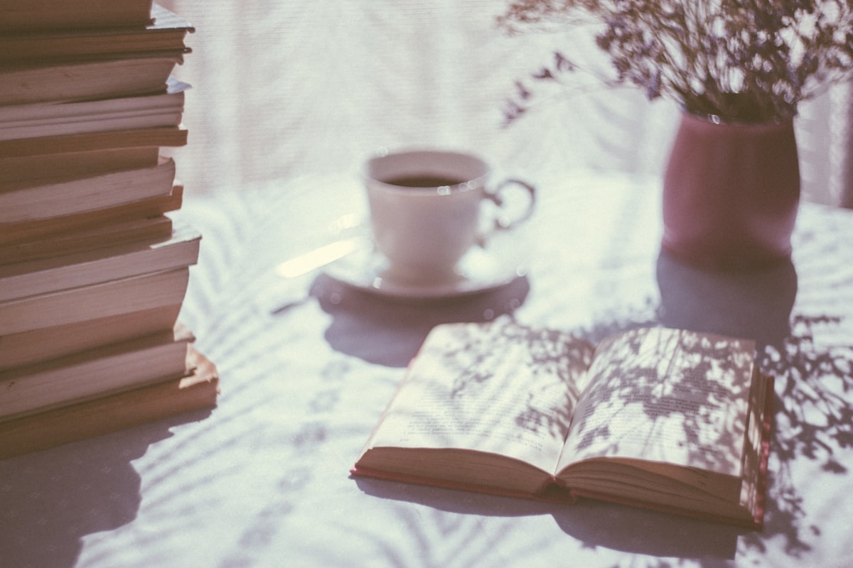 An open book beside a white ceramic teacup on a saucer in morning light
