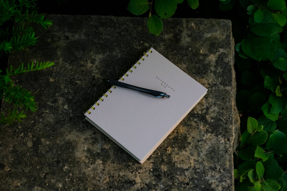 An open notebook resting on grass beside a fallen leaf and a pen, used as a nature journaling example