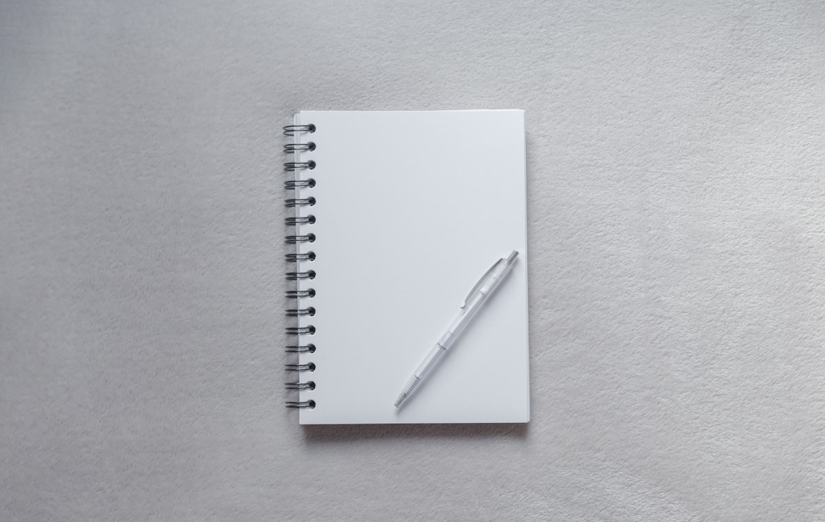 A white notebook lying open with a pen resting on top, ready for a photo journal entry