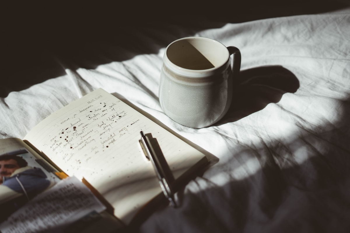 A person writing slowly in a journal, a cup of tea beside them, soft morning light across the page