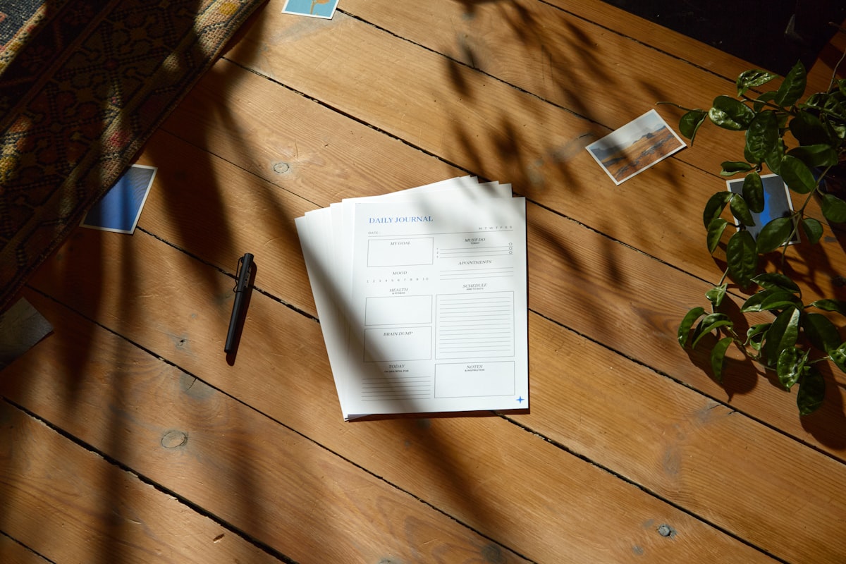An open notebook resting on a sunlit wooden table beside a glass of water, with warm summer light falling across the page