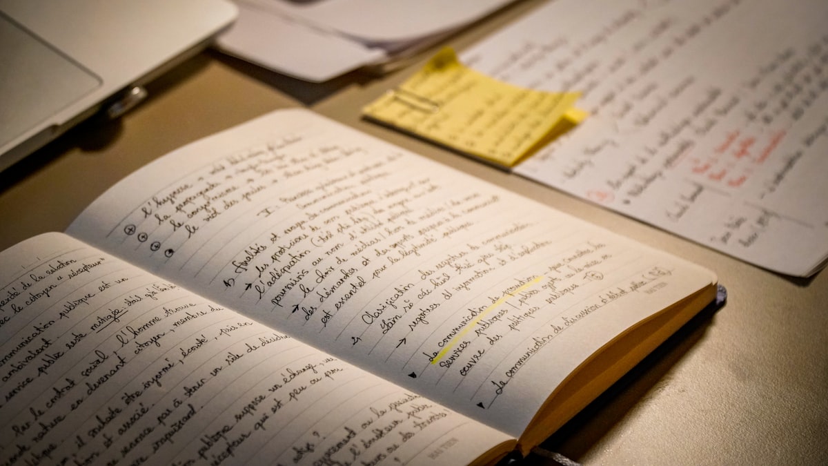 An open notebook covered in dense handwritten notes with a pen resting across the page