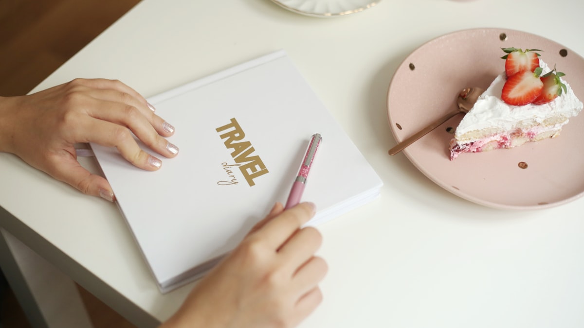 An open notebook on a wooden table with a pen, tea cup, and travel items scattered nearby