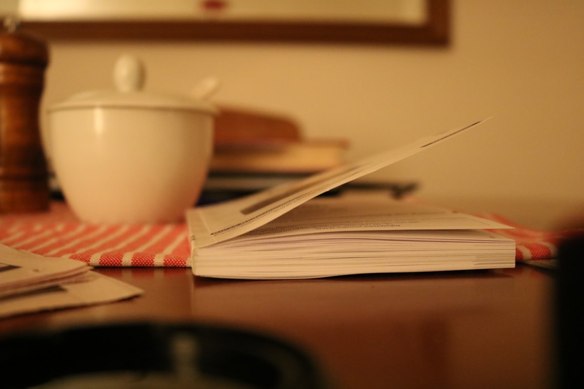 An open notebook on a wooden table with a cup of tea beside it and afternoon light falling across the page