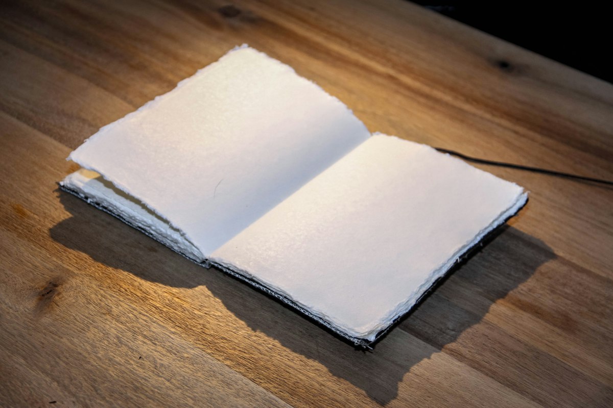 A small handmade booklet with deckled paper edges lying open on a wooden table